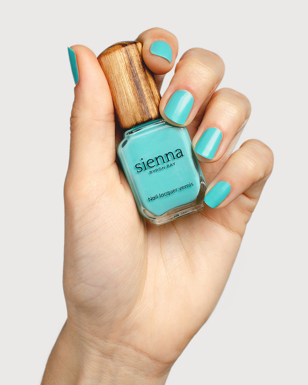 Turquoise aqua nail polish hand swatch on fair skin tone holding a sienna bottle