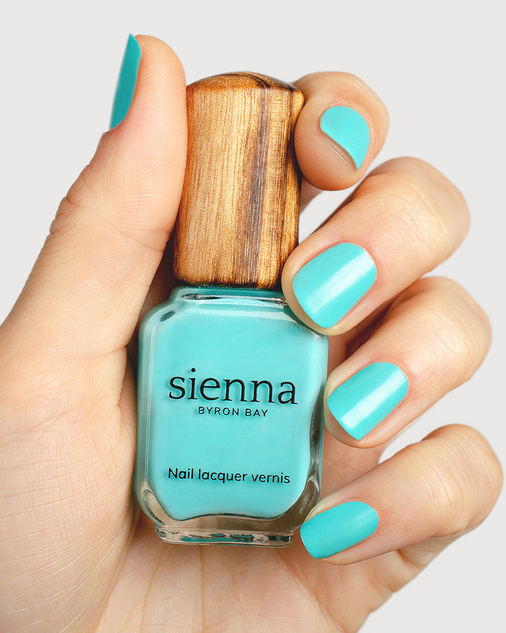 Turquoise aqua nail polish hand swatch on fair skin tone holding a sienna bottle close up