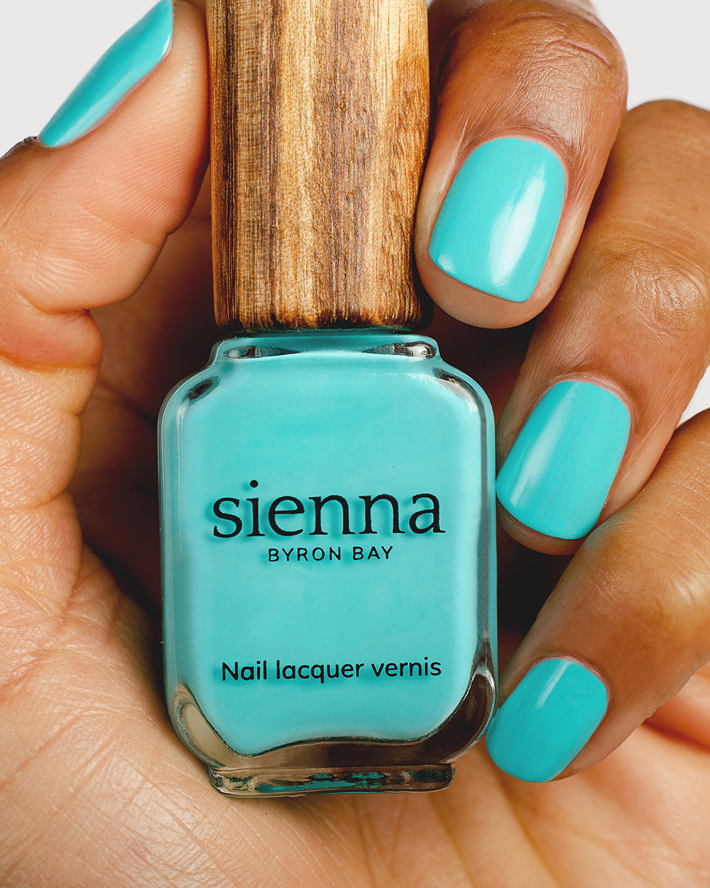 Turquoise aqua nail polish hand swatch on medium skin tone holding a sienna bottle