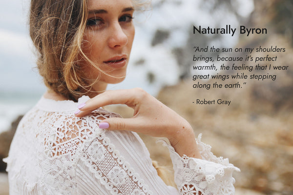 Woman with fair skin tone wearing Bohemian nail polish at Byron Bay beach with text Naturally Byron and quote.