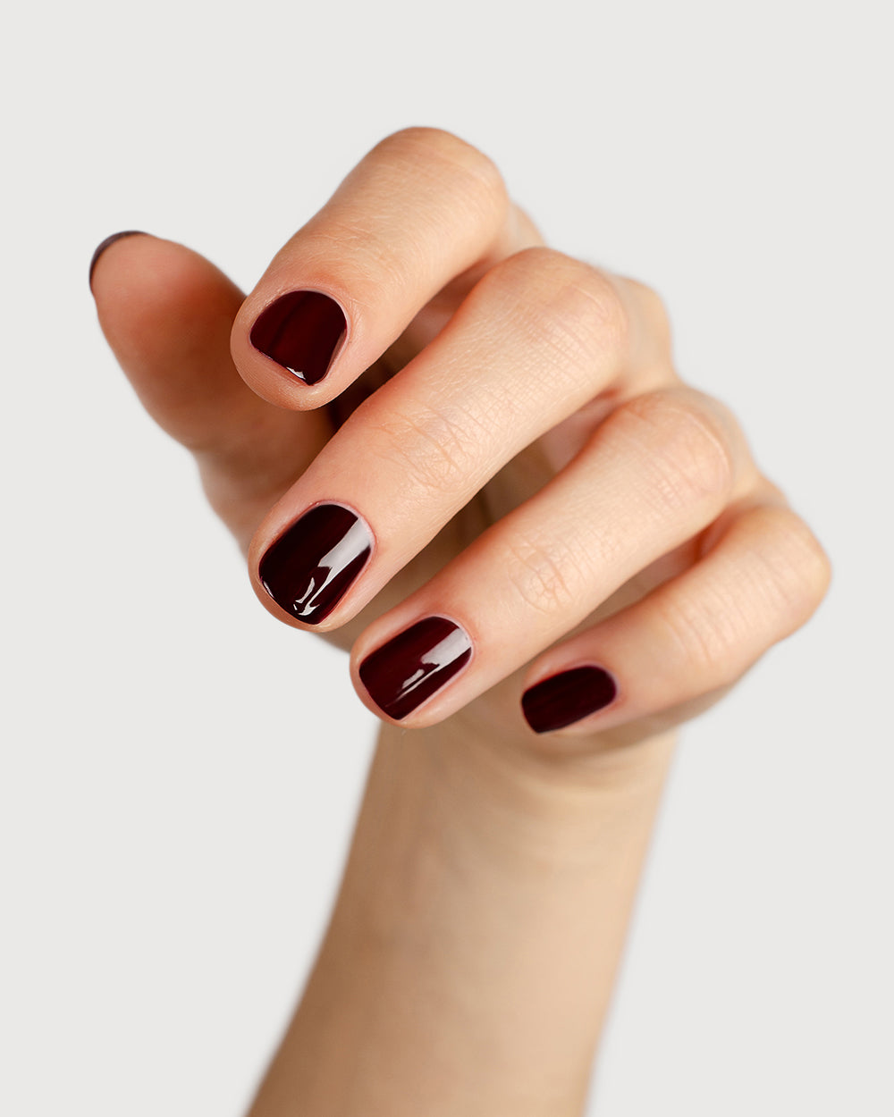 dark red nail polish hand swatch on fair skin tone holding a sienna bottle