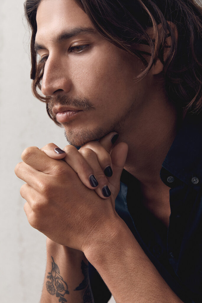 young man day dreaming and holding his face with his hands wearing dark aubergine nail polish