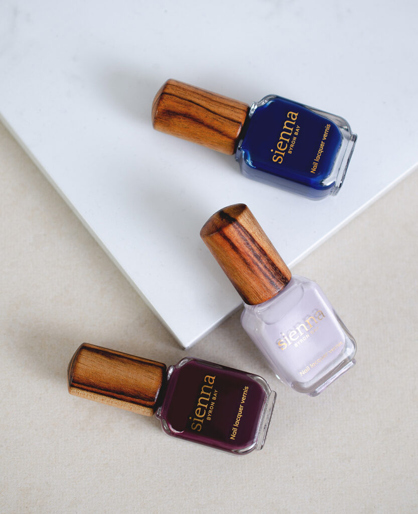 top shot of dark purple navy blue and pastel purple-grey nail polish bottles with timber cap by sienna