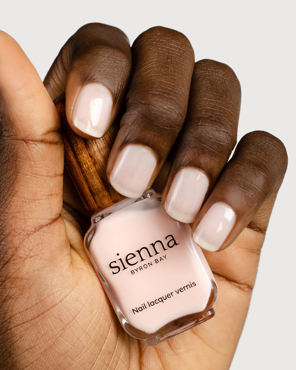 light rosewater pink sheer nail polish hand swatch on dark skin tone holding sienna bottle close up