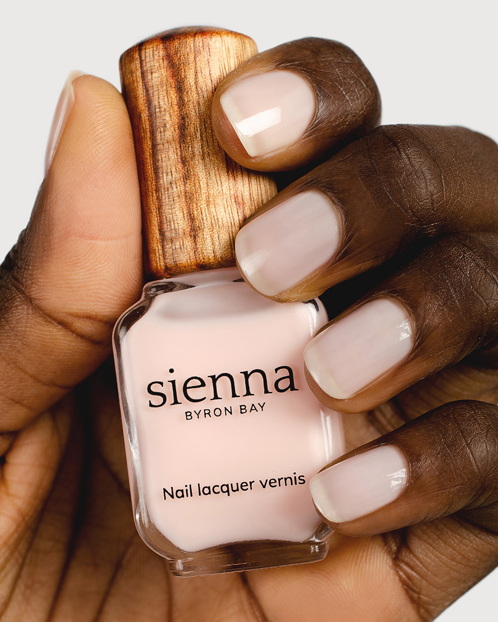 light rosewater pink sheer nail polish hand swatch on dark skin tone holding sienna bottle close up