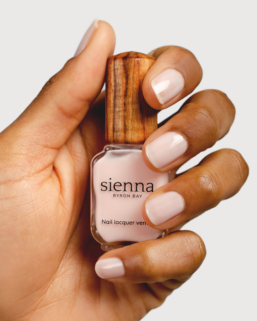 light rosewater pink sheer nail polish hand swatch on medium skin tone holding sienna bottle