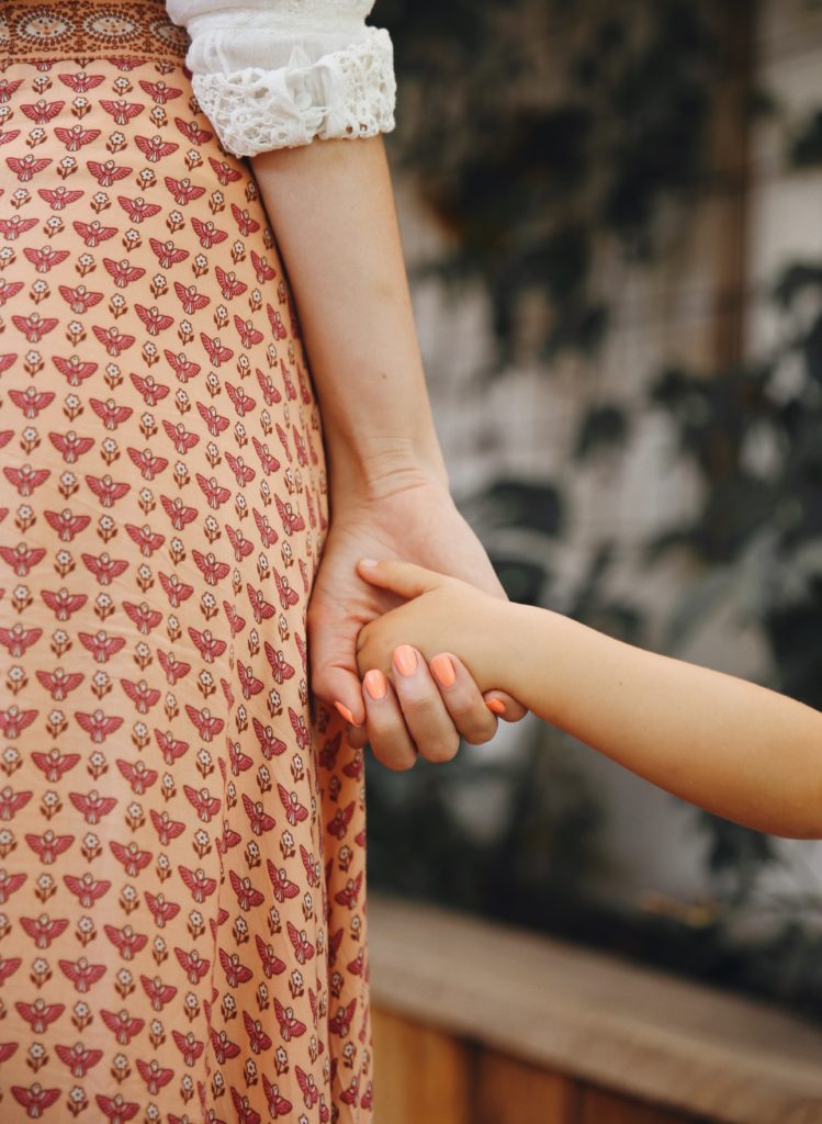 woman's hand wearing bright peach nail polish by sienna and holding child's hand