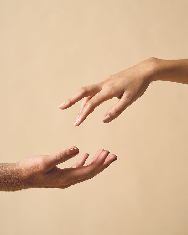 man hand and woman hand connecting wearing red nail polish and pink nail polish on beige background