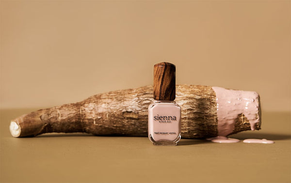 light pink nail polish bottle and nail polish dripping on cassava on nude background by sienna