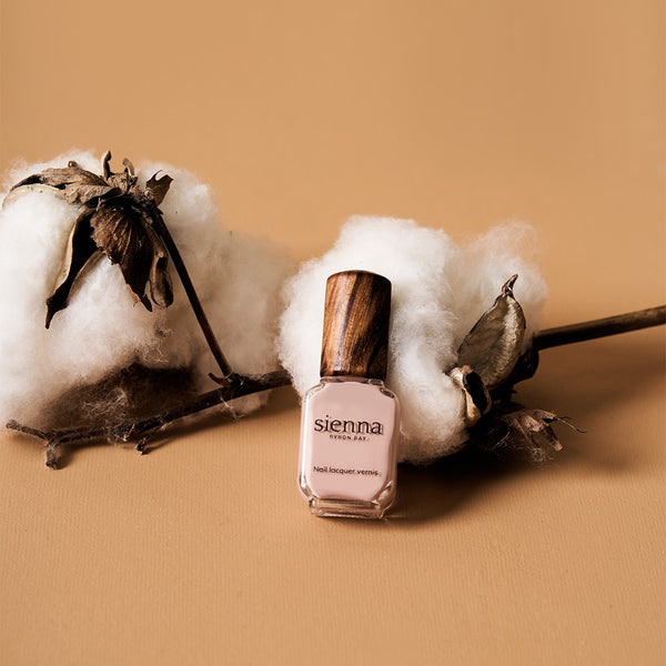 light pink nail polish bottle place on cotton ball on peach background by sienna