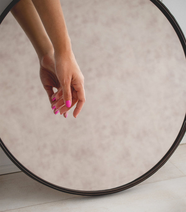 hand in front of a round mirror wearing fushia nail polish
