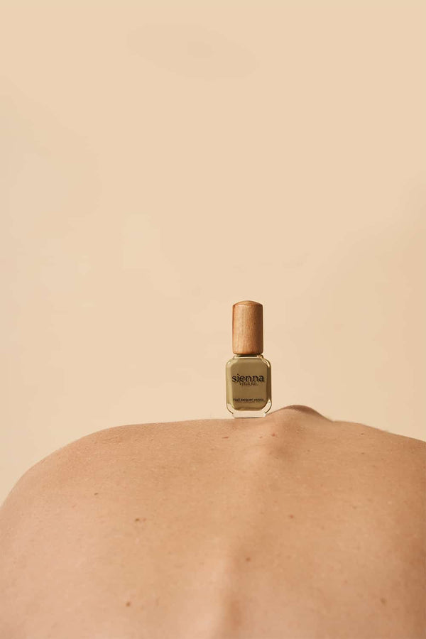green nail polish bottle with wooden cap sitting on top of the bare skin back of young man