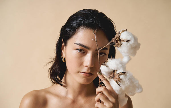 young bare skin woman holding cotton branch and wearing green nail polish by sienna on beige background