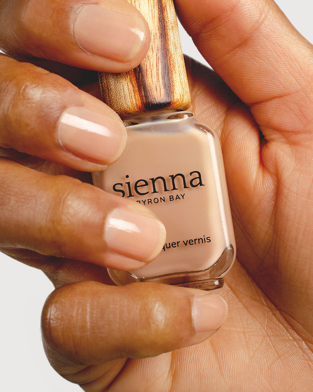 nude sheer nail polish hand swatch on medium skin tone holding a sienna bottle up close