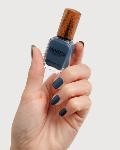 blue-grey nail polish hand swatch on fair skin tone holding a sienna bottle