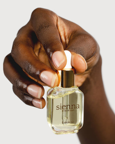 dark skin tone hand holding bottle of cuticle oil