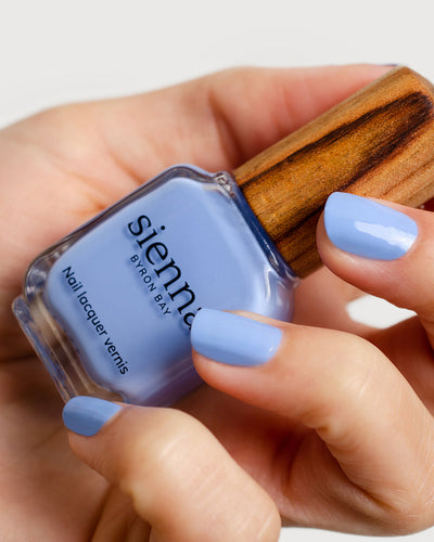 periwinkle blue nail polish hand swatch on fair skin tone holding a sienna bottle up close