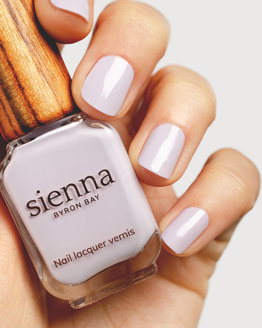 Pastel purple-grey nail polish hand swatch on fair skin tone holding a sienna bottle up close