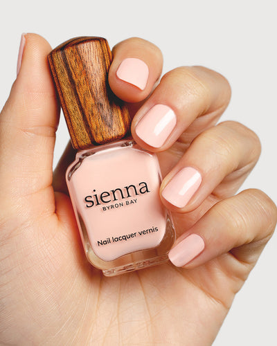 pastel pink nail polish hand swatch on fair skin tone holding a sienna bottle