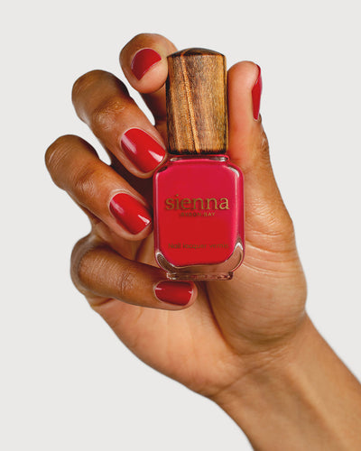 classic red nail polish hand swatch on medium skin tone holding a sienna bottle
