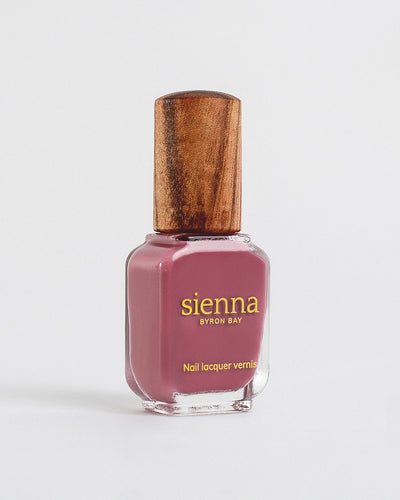 Heartspace raspberry sorbet crème Sienna nail polish bottles with with gold logo and timber lids on a light grey-cream background.