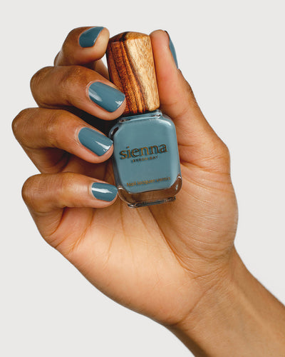 Mid grey-blue nail polish hand swatch on medium skin tone holding sienna bottle