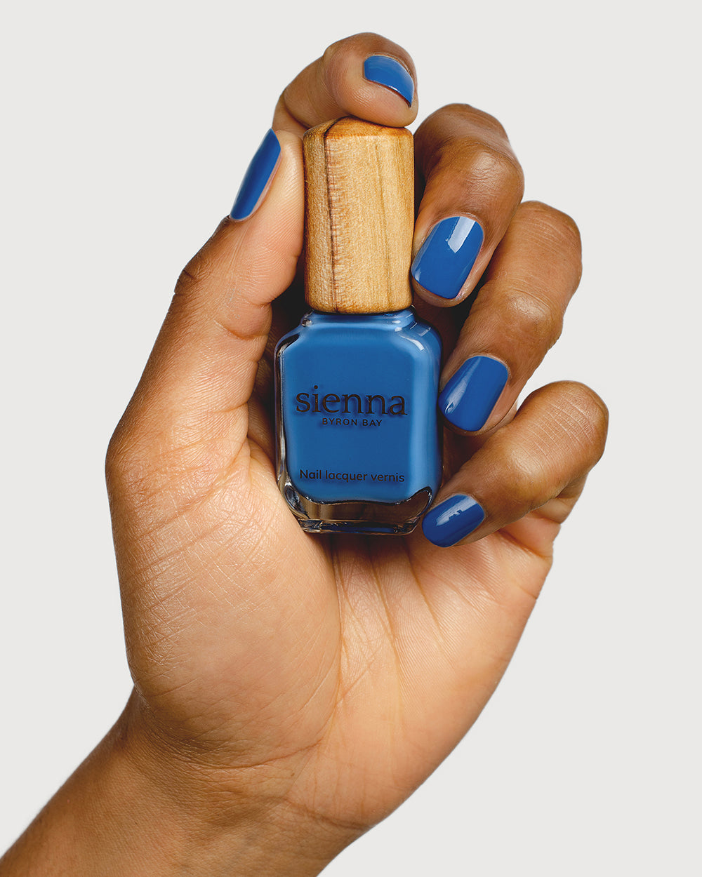 electric blue nail polish hand swatch on medium skin tone holding sienna bottle