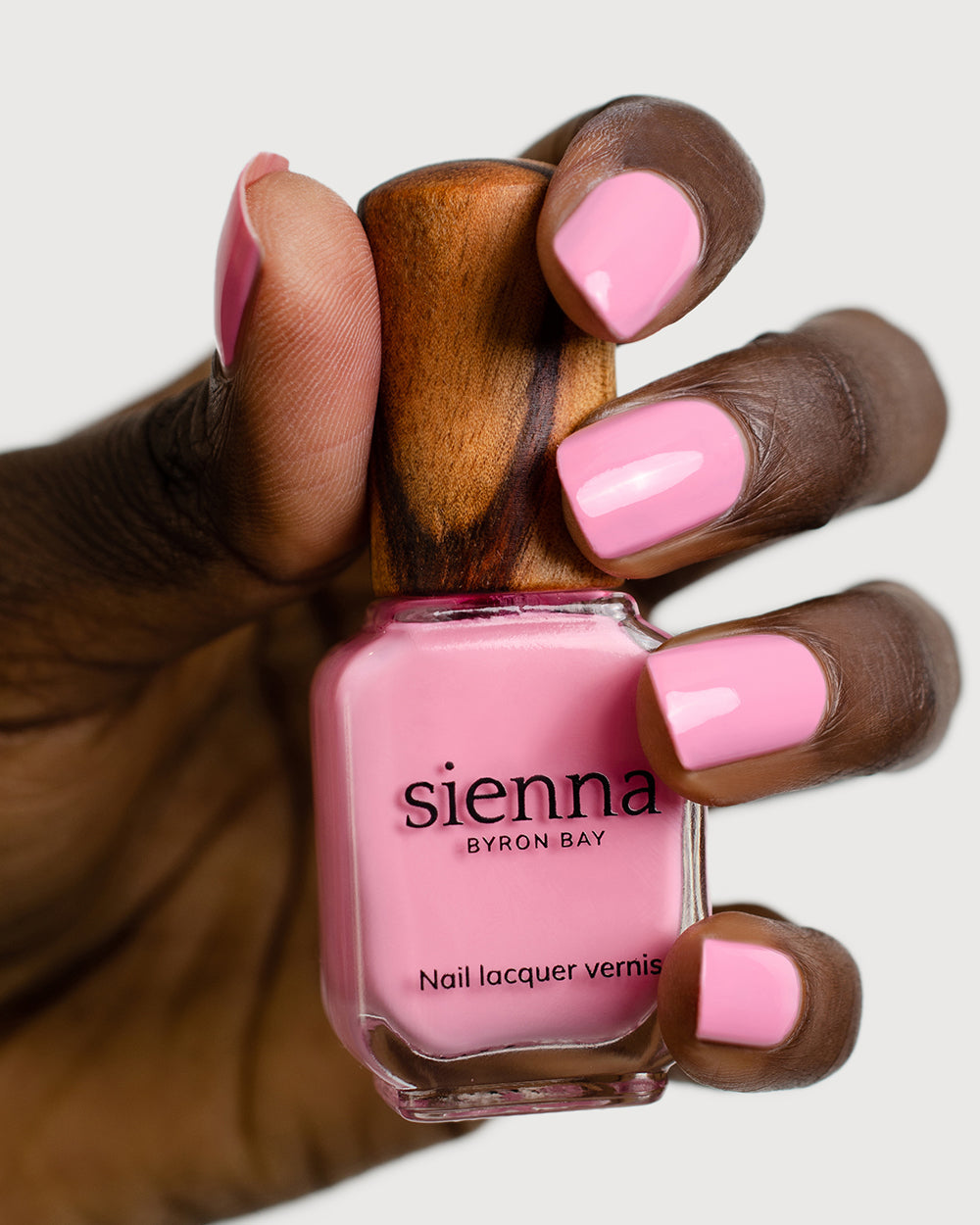Classic lolly pink nail polish hand swatch on dark skin tone holding sienna bottle close-up