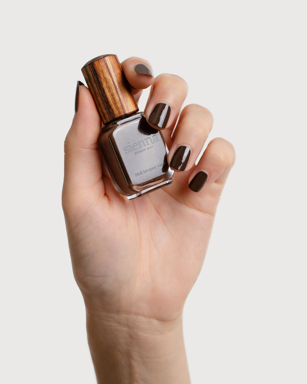 chocolate brown nail polish hand swatch on fair skin tone holding sienna bottle