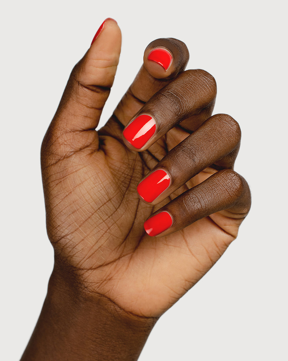 bright red nail polish hand swatch on dark skin tone