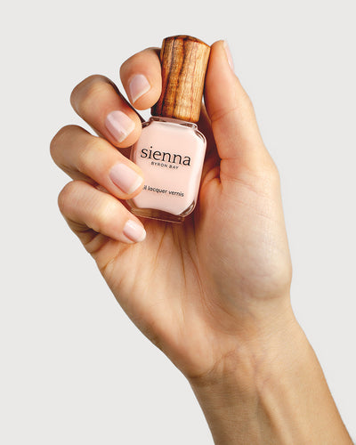 light rosewater pink sheer nail polish hand swatch on fair skin tone holding sienna bottle