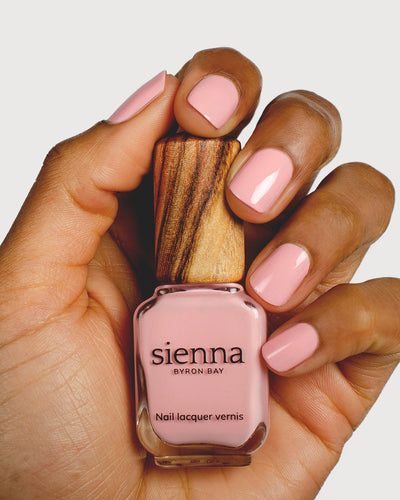 Cherry blossom pink nail polish hand swatch on medium skin tone holding sienna bottle