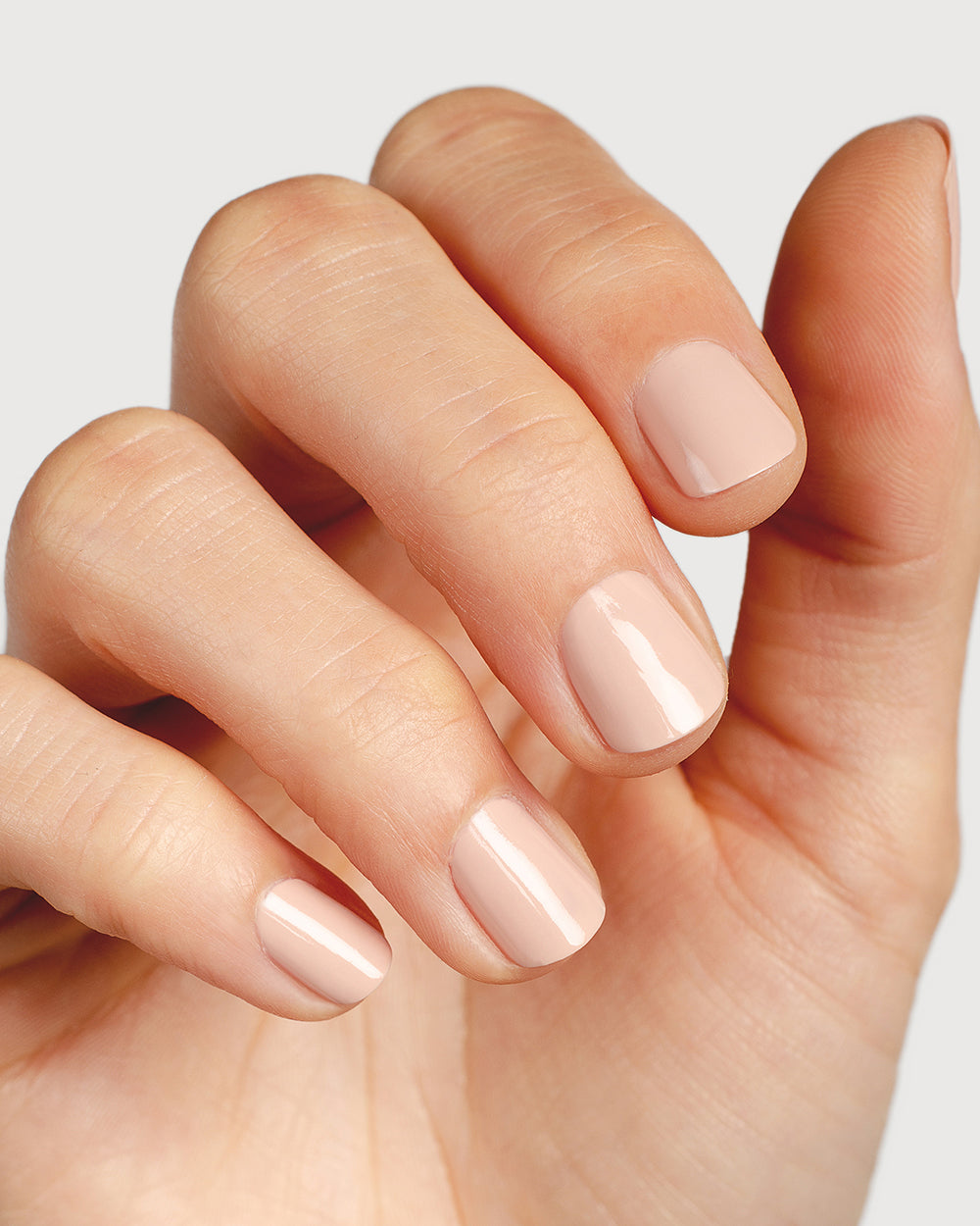 Soft neutral-pink nail polish hand swatch on fair skin tone up-close