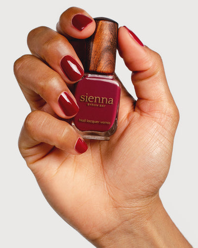 Plum red nail polish hand swatch on medium skin tone holding sienna bottle