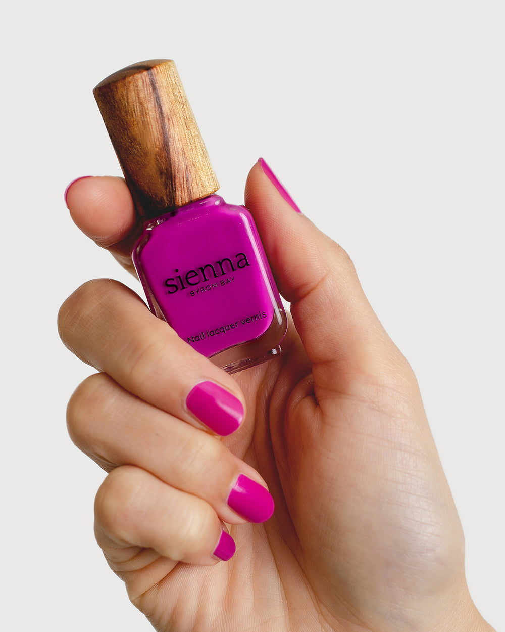 Bright magenta nail polish hand swatch on fair skin tone holding sienna bottle close-up
