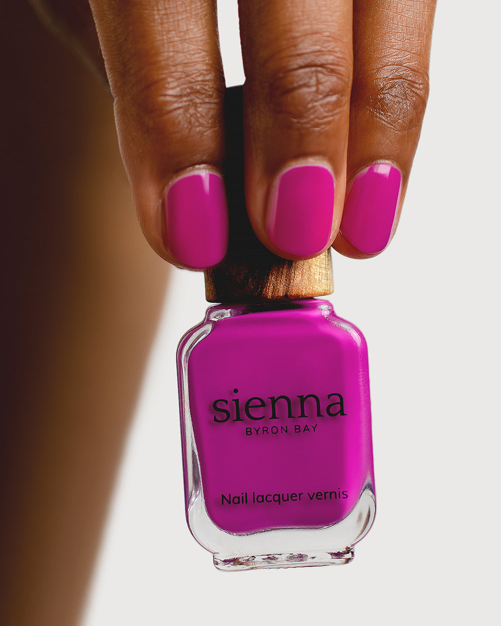 Bright magenta nail polish hand swatch on medium skin tone holding sienna bottle close-up