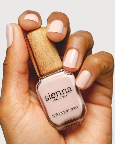 Light champagne pink nail polish hand swatch on medium skin tone holding sienna bottle