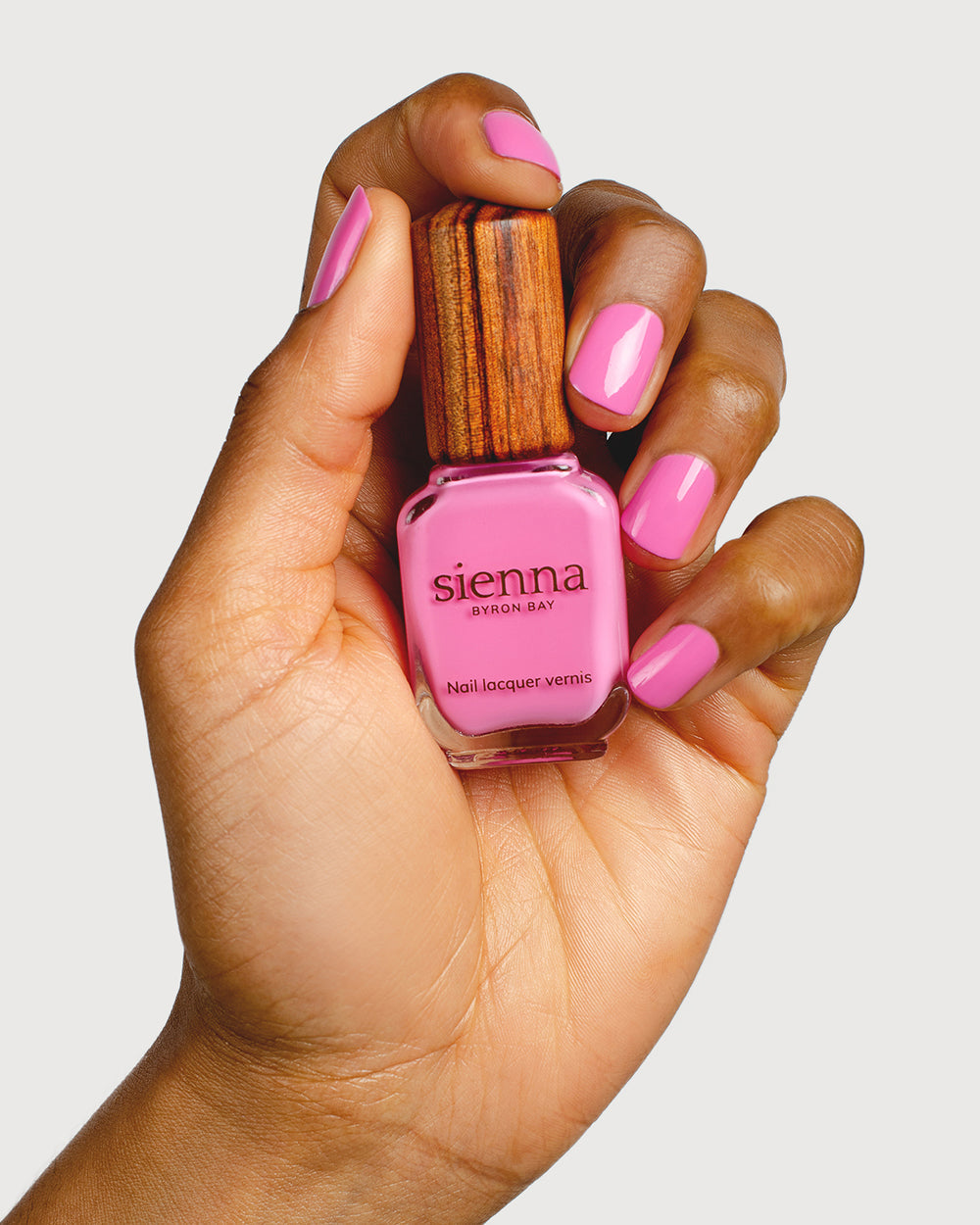 Bright mid-tone fuchsia nail polish hand swatch on medium skin tone holding sienna bottle
