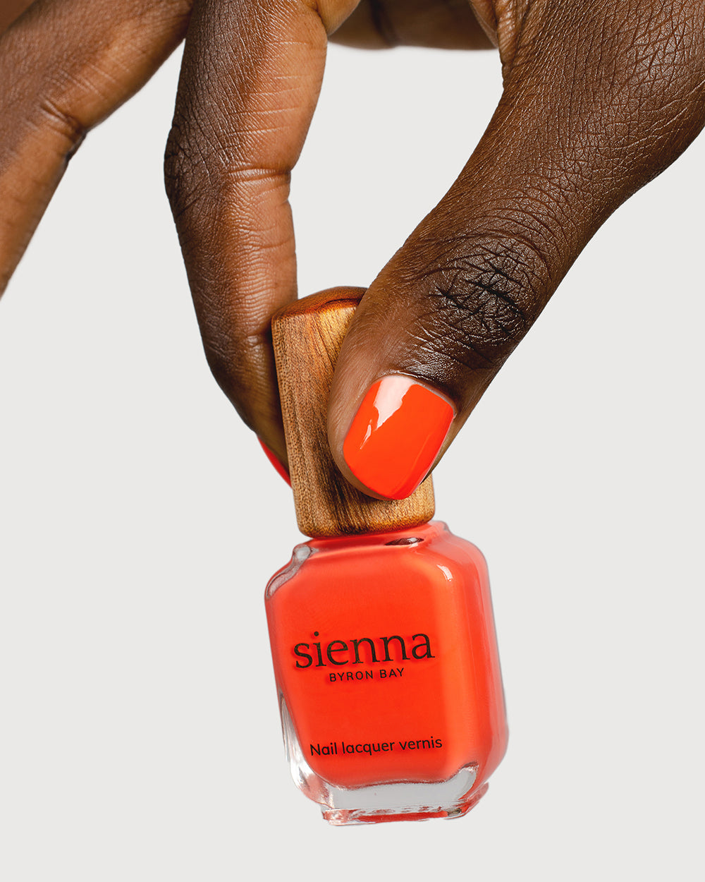 Tangerine nail polish hand swatch on dark skin tone holding sienna bottle
